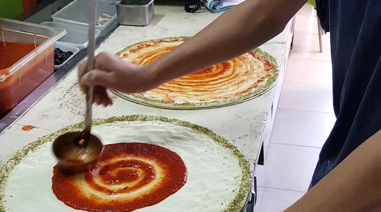רוטב נמרח ביד על בצק פיצה במטבח של פיצה אוליב